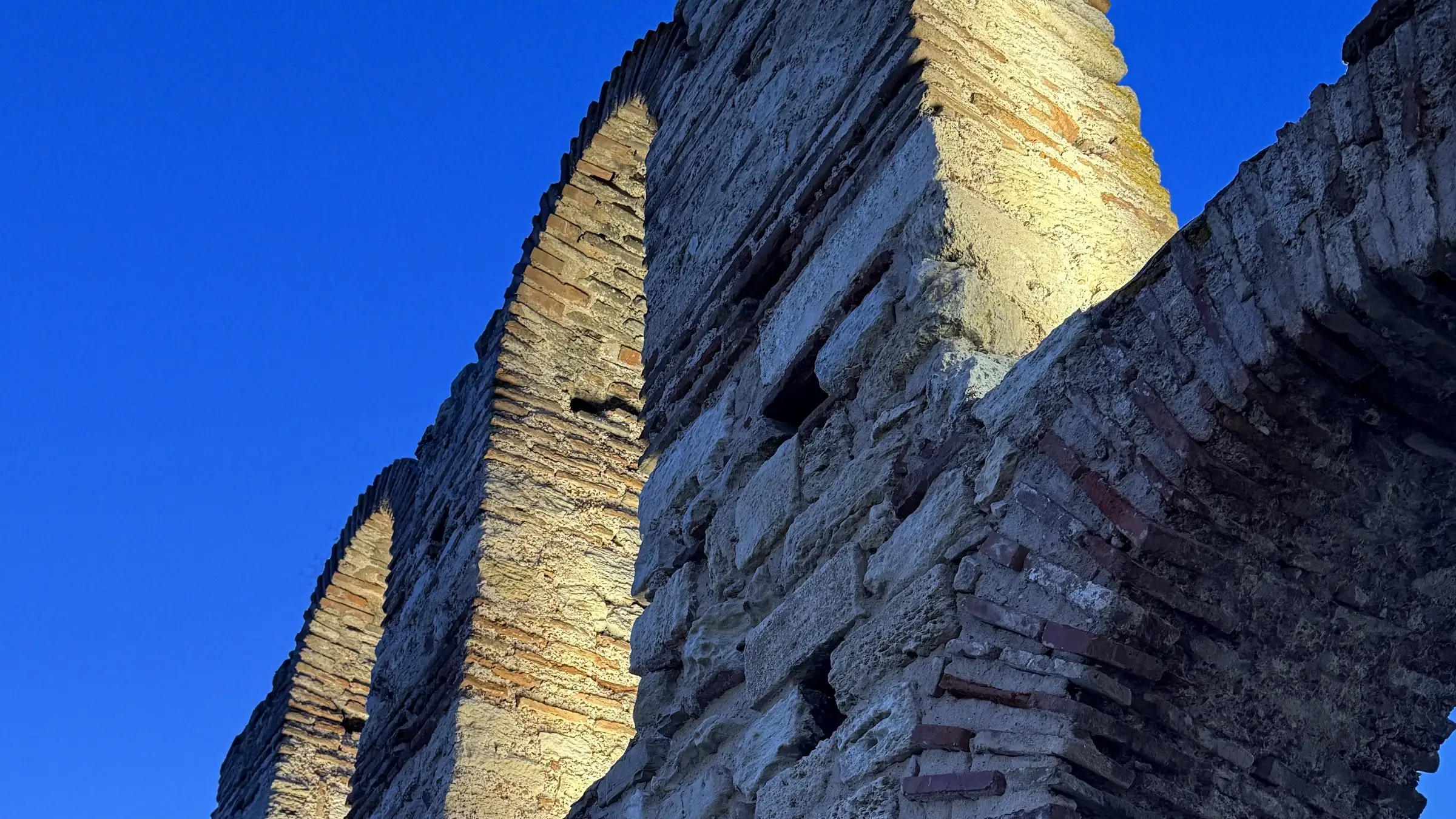 The arcade of the Old Metropolitan basilica in Nessebar, its stone lit low against a deep blue sky